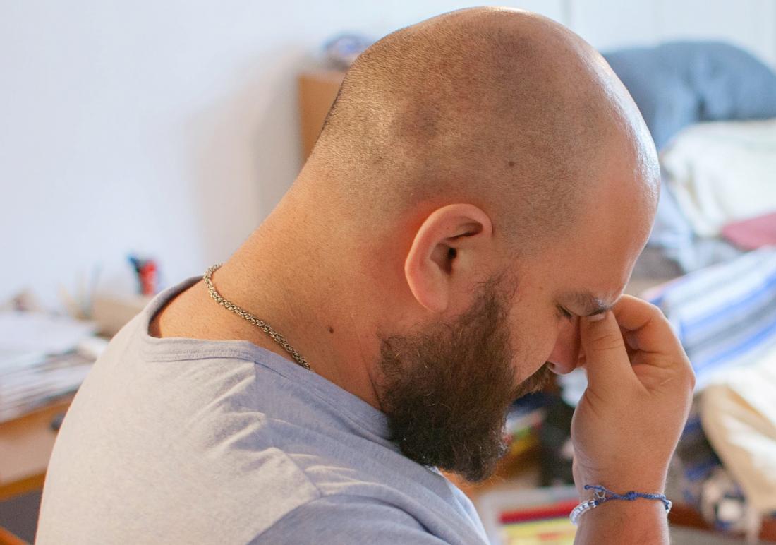 Bald man experiencing headache and stress pinching bridge of nose.