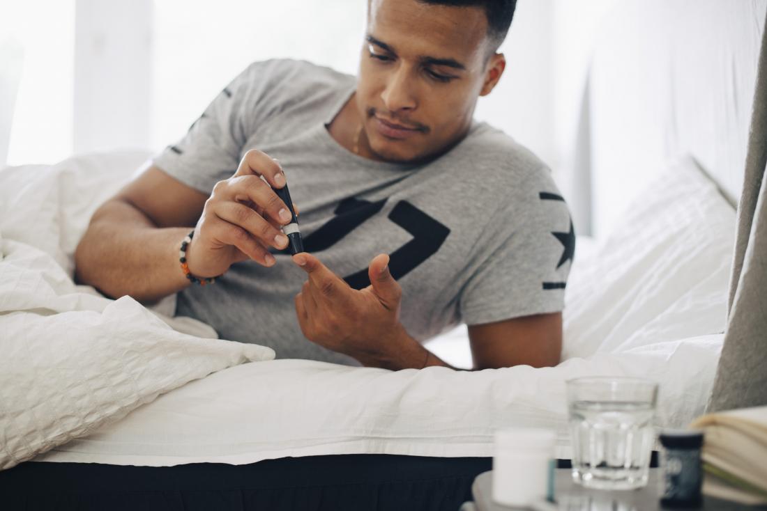 man checking his blood sugar levels in bed