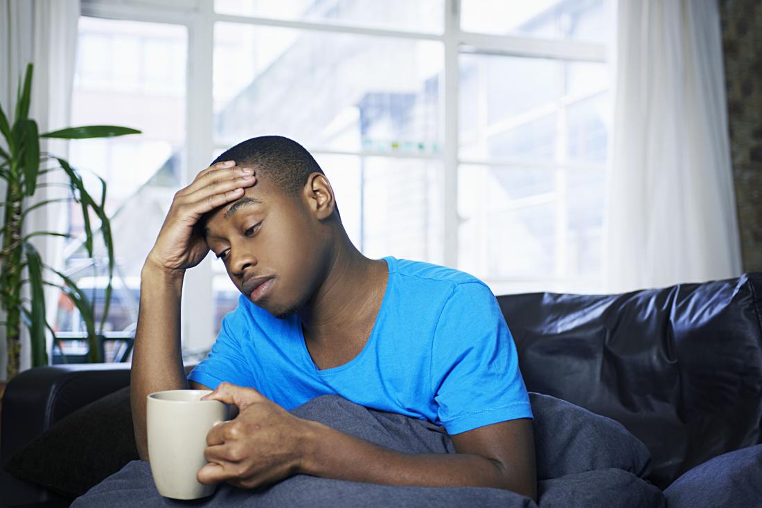 Tired man under blanket holding mug