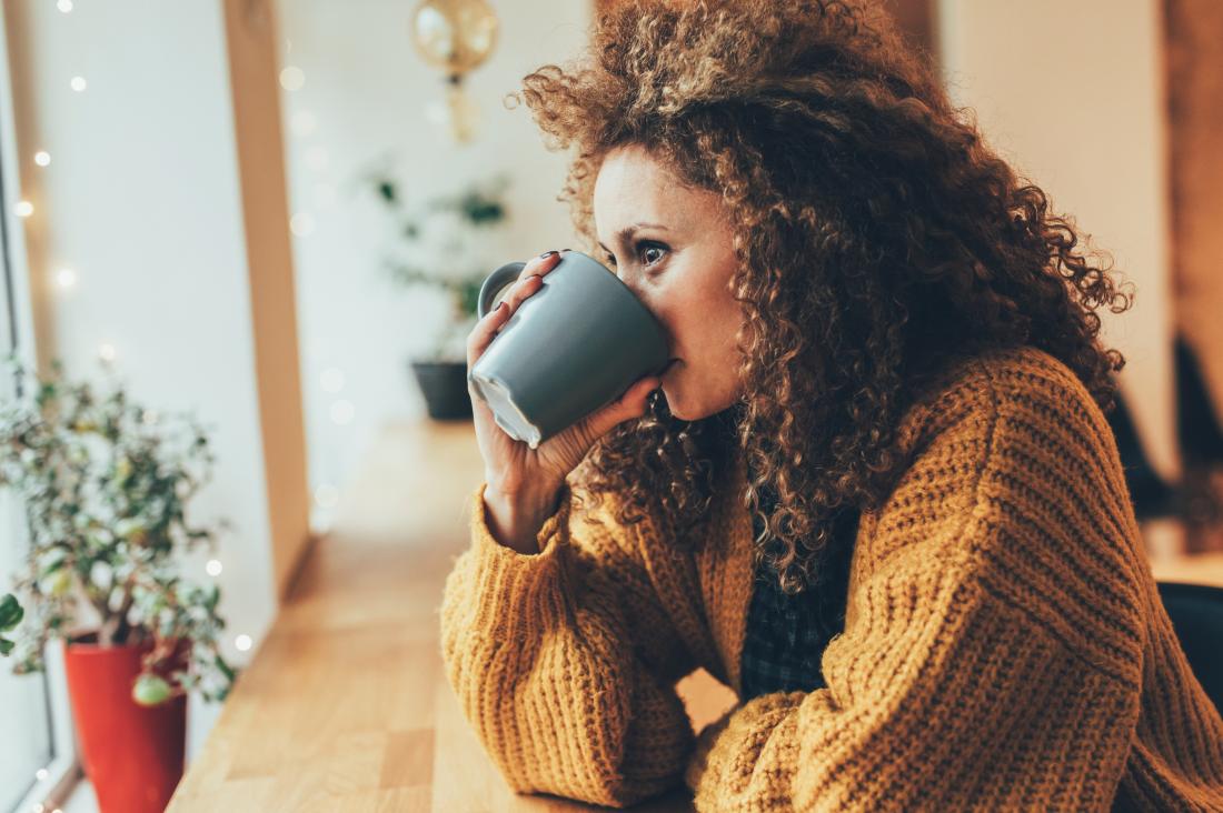 Woman drinking hot drink from mug in cafe.