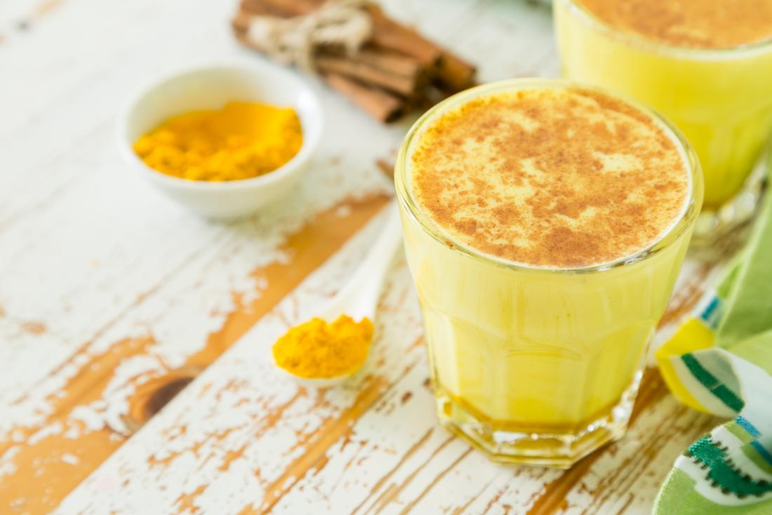 Golden milk turmeric tea in glass on wooden table