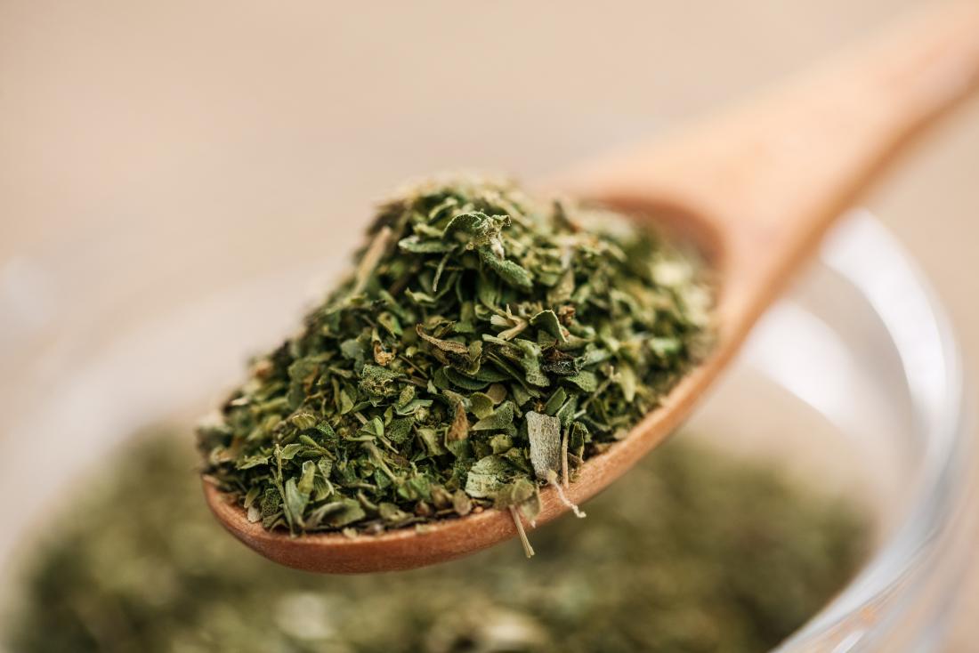 Dried oregano on wooden spoon.